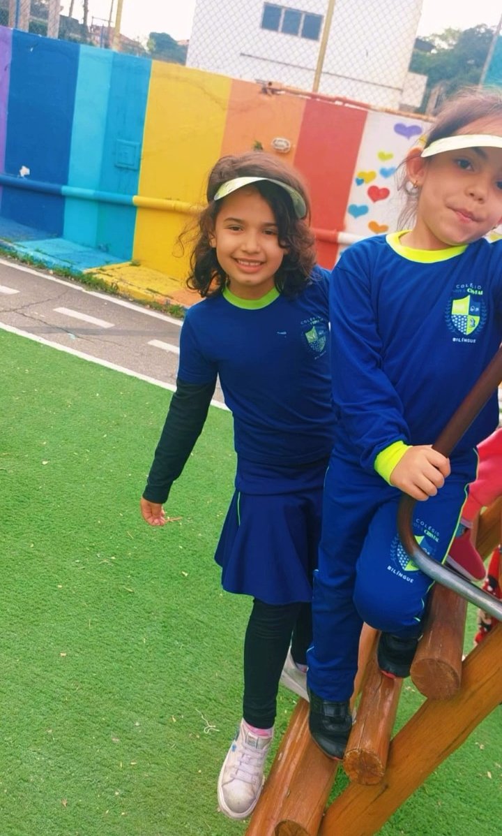 Duas alunas da Escola Cristal, de uniforme azul, sorrindo no playground da escola