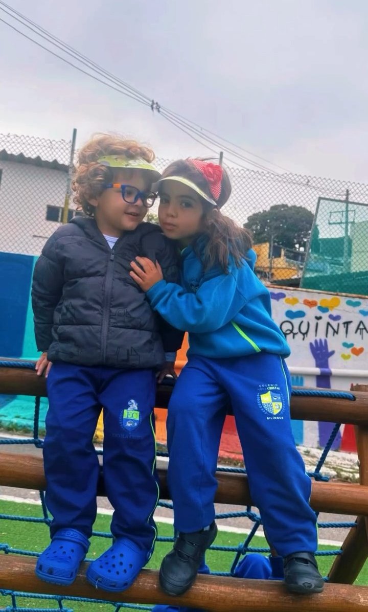 Dois alunos abraçados no trepa-trepa, com o mural do quintal ao fundo